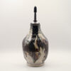 Ceramic oil bottle in glossy black and cream glaze with rust streaks, fitted with a metal pour spout and black cap