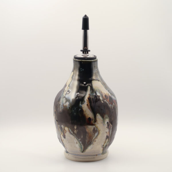Ceramic oil bottle in glossy black and cream glaze with rust streaks, fitted with a metal pour spout and black cap