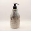 Ceramic soap dispenser in speckled cream glaze with a drippy blue, purple and amber top and a black pump