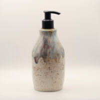Ceramic soap dispenser in speckled cream glaze with a drippy blue, purple and amber top and a black pump
