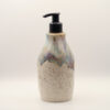 Ceramic soap dispenser with black pump, speckled cream glaze below a dripping blue, purple and amber glaze at the top