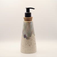 Tapered ceramic soap dispenser in speckled cream glaze with blue, purple and amber drips at the top, cork collar and black pu