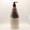 Tall ceramic soap bottle in cream glaze with blue, red and copper drips around the top, black pump in a cork stopper