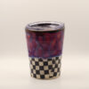 Ceramic travel cup with clear plastic lid, red and purple drippy glaze over a black and white checkerboard base
