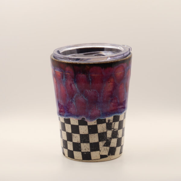 Ceramic travel cup with clear plastic lid, red and purple drippy glaze over a black and white checkerboard base
