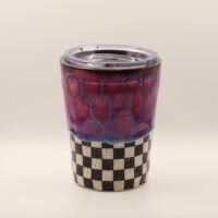 Ceramic travel cup with clear plastic lid, red and purple drippy glaze on top and black and white speckled checkerboard base