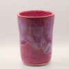 Handleless ceramic cup in pink glaze with lilac drips in a wavy band, speckled clay and unglazed base