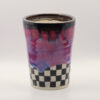 Ceramic tumbler with a dark rim, dripping pink and lavender glaze, and a black and white checkerboard base