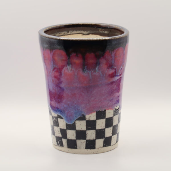 Ceramic tumbler with a dark rim, dripping pink and lavender glaze, and a black and white checkerboard base
