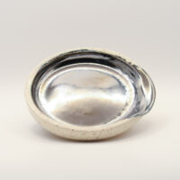 Round spoon rest with a mirror-like metallic silver glaze inside, a pinched notch at the rim and a speckled cream exterior