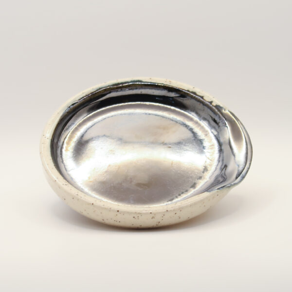Round spoon rest with a mirror-like metallic silver glaze inside, a pinched notch at the rim and a speckled cream exterior