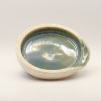 Round spoon rest with a glossy blue-green glazed interior, speckled cream exterior and a notch in the rim for a handle