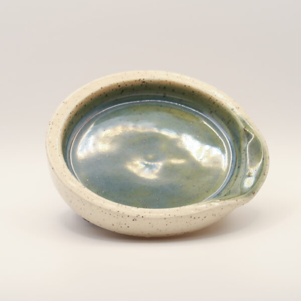 Round spoon rest with a glossy blue-green glazed interior, speckled cream exterior and a notch in the rim for a handle