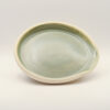 Shallow oval spoon rest with a pale sage green glaze inside, an unglazed cream rim and a pinched notch on one side