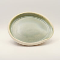 Shallow oval spoon rest with a pale sage green glaze inside, an unglazed cream rim and a pinched notch on one side