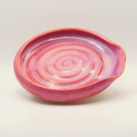 Ceramic spoon rest in pink and lilac glaze with a carved spiral in the base and a pinched notch at one end