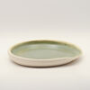 Shallow ceramic spoon rest with a sage green glazed interior, unglazed cream exterior and a pinched spout on one side