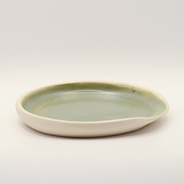 Shallow ceramic spoon rest with a sage green glazed interior, unglazed cream exterior and a pinched spout on one side