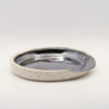 Shallow round spoon rest with a glossy metallic black-silver glazed interior and a speckled cream exterior and rim