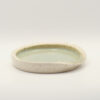 Shallow speckled cream stoneware spoon rest with a pale green glazed interior and a notch in the rim, on a white background