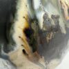 Close-up of an oil bottle's glazed surface in cream, amber, and pale blue with dark metallic speckled patches