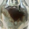Close-up of a ceramic oil bottle with dark brown, sea green and cream flowing glazes and a silvery sheen