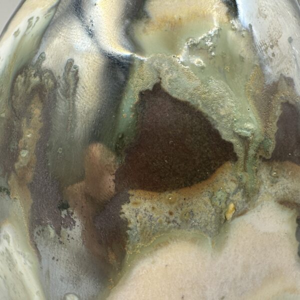 img_7924 Close-up of a soap bottle's dimpled surface in glossy sage green, cream and silvery glaze with patches of matte dark brown