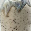 Close-up of a speckled cream ceramic soap bottle with a blue, purple and gold glaze dripping down from the shoulder