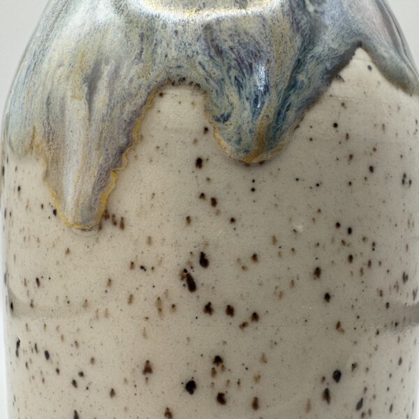 Close-up of a speckled cream ceramic soap bottle with a blue, purple and gold glaze dripping down from the shoulder