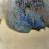 Close-up of a soap bottle's blue, rust and grey speckled glaze dripping over bare cream speckled clay
