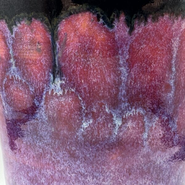 Close-up of a cup's glaze, dark brown drips at the top over red and pink with purple and pale blue streaks